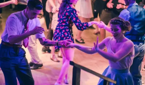 Coppie che ballano lo swing in una sala affollata, con abiti in stile anni Cinquanta.