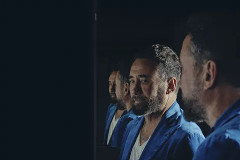 Federico Zampaglione dei Tiromancino, in giacca blu, davanti a uno specchio che moltiplica la sua immagine